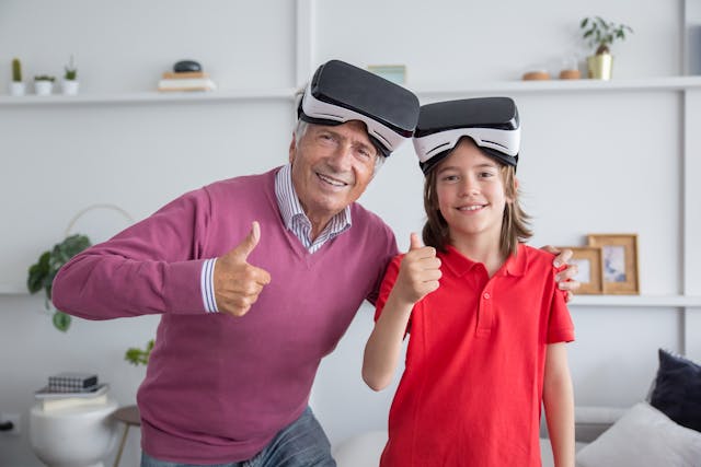 un abuelo y su nieto, con unas gafas para ver 3D miran a la cámara con el pulgar levantado y sonriendo