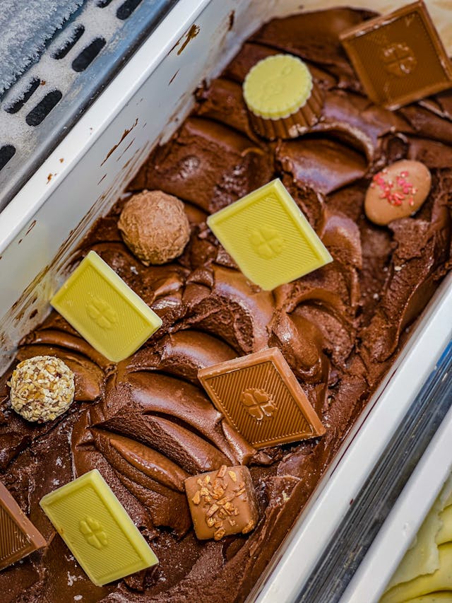 Helado artesanal de chocolate cremoso decorado con bombones y tabletas de chocolate en vitrina de heladería