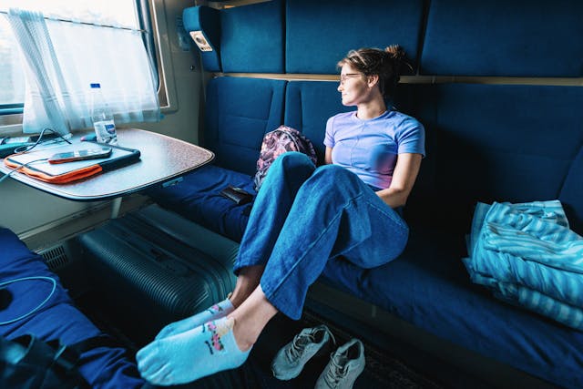 una chica viaja en tren. Está en vagón, con los pies con calcetines sobre el asiento, relajada. Ella mira a través de la ventana