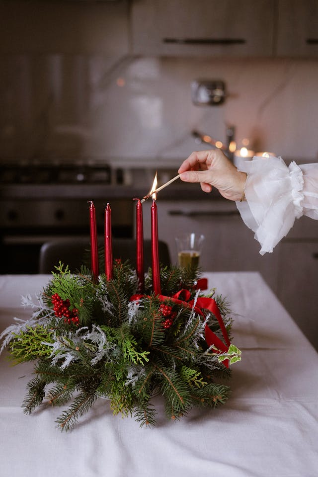 Una mano está encendiendo unas velas rojas en una mesa preparada para Navidad