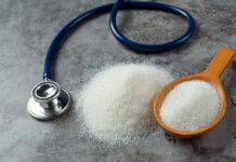 Una mesa con una cuchara que contiene azñucar blanca y al lado hay un estetoscopio