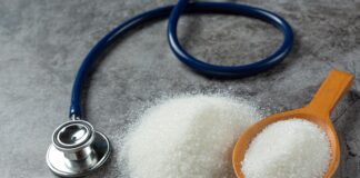 Una mesa con una cuchara que contiene azñucar blanca y al lado hay un estetoscopio