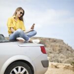 una chica sobre el capó de su coche descapotable, monitorizando su glucosa.
