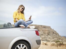 una chica sobre el capó de su coche descapotable, monitorizando su glucosa.
