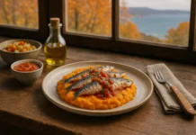 Un plato con sardinas sobre una base de puré de verduras o boniato. Al lado de una ventana, y al fondo se ve el mar y un paisaje otoñal