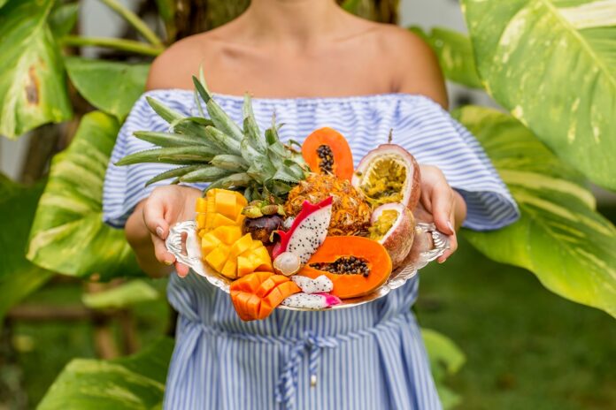 Recomendaciones sobre el consumo de frutas tropicales en la diabetes Bandeja sostenida por una mujer joven con frutas exóticas y tropicales, so
