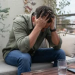 Persona con estrés emocional sentada en la terraza de casa, con la cabeza entre las manos, representando el burnout en diabetes y el agotamiento mental cotidiano