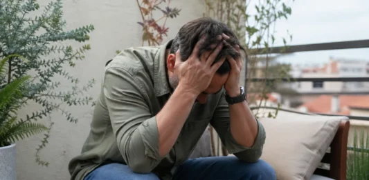 Persona con estrés emocional sentada en la terraza de casa, con la cabeza entre las manos, representando el burnout en diabetes y el agotamiento mental cotidiano