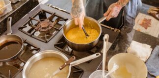 Una cocina, donde se intuye la mano del cocinero. Tiene al fuego hasta 3 calderos donde se está cocinando varios caldos