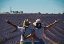 Dos mujeres de espaldas, con los brazos en alto, abrazadas en un campo de lavanda al atardecer.