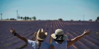 Dos mujeres de espaldas, con los brazos en alto, abrazadas en un campo de lavanda al atardecer.