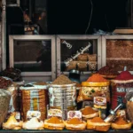 Puesto de mercado con diferentes especias a granel en recipientes y sacos, como cúrcuma, pimentón y mezclas aromáticas utilizadas en la cocina.