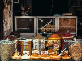 Puesto de mercado con diferentes especias a granel en recipientes y sacos, como cúrcuma, pimentón y mezclas aromáticas utilizadas en la cocina.