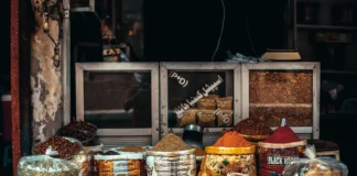 Puesto de mercado con diferentes especias a granel en recipientes y sacos, como cúrcuma, pimentón y mezclas aromáticas utilizadas en la cocina.