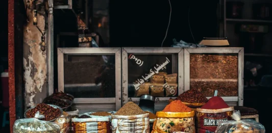 Puesto de mercado con diferentes especias a granel en recipientes y sacos, como cúrcuma, pimentón y mezclas aromáticas utilizadas en la cocina.