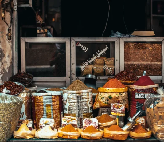 Puesto de mercado con diferentes especias a granel en recipientes y sacos, como cúrcuma, pimentón y mezclas aromáticas utilizadas en la cocina.