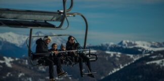 Una familia joven, con sus dos niños pequeños van en una telesilla, subiendo a las pista de esquí