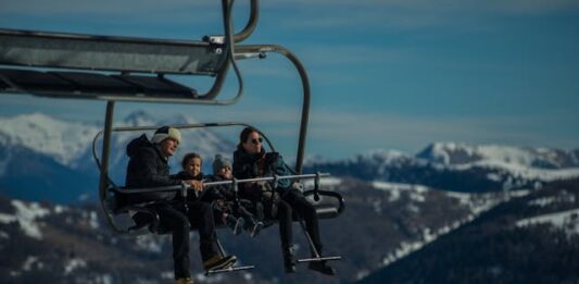 Una familia joven, con sus dos niños pequeños van en una telesilla, subiendo a las pista de esquí