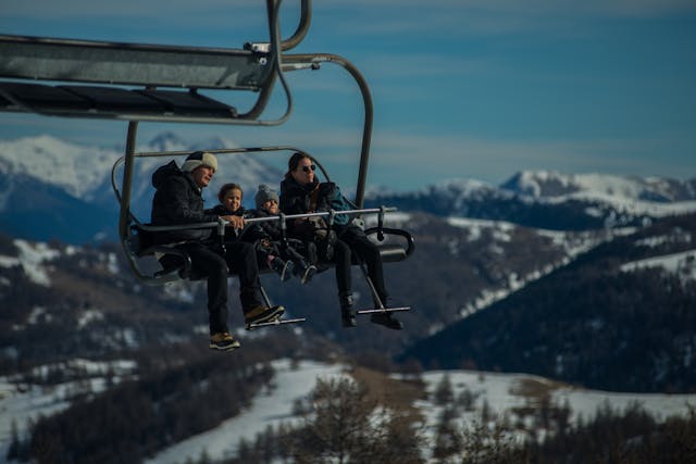 Una familia joven, con sus dos niños pequeños van en una telesilla, subiendo a las pista de esquí