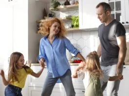 Familia con dos niñas bailando y divirtiéndose en la cocina de casa, mostrando un momento cotidiano de actividad física y bienestar en familia.