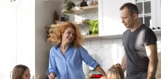 Familia con dos niñas bailando y divirtiéndose en la cocina de casa, mostrando un momento cotidiano de actividad física y bienestar en familia.