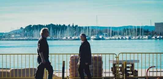 En un paseo marítimo se ven a dos personas, hombres paseando o caminando