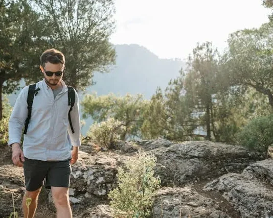 Un hombre joven con gafas caminando en el monte.