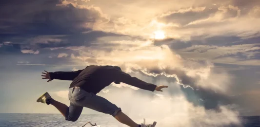 un hombre saltando, sobre un pavimento y un cielo nublado, y un reloj antiguo marcando el tiempo