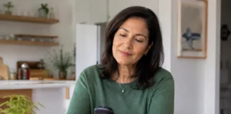 Mujer de mediana edad consulta un medidor de glucosa en casa durante su rutina diaria de autocontrol de la diabetes.
