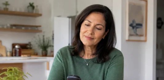 Coma diabético: qué es, por qué ocurre y cómo prevenirlo Mujer de mediana edad consulta un medidor de glucosa en casa durante su rutina diaria de autocontrol de la diabetes.