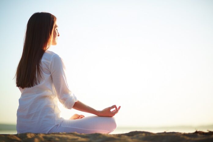 Como usar la meditación para relajación de personas con diabetes Una mujer meditando en posición de lotus al aire libre