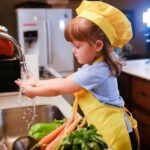 Una niña con delantal amarillo delante de un fregadero, lista parece para ponerse a cocinar