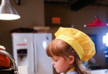 Una niña con delantal amarillo delante de un fregadero, lista parece para ponerse a cocinar