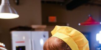 Una niña con delantal amarillo delante de un fregadero, lista parece para ponerse a cocinar