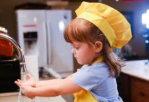 Una niña con delantal amarillo delante de un fregadero, lista parece para ponerse a cocinar