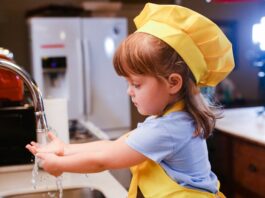 Una niña con delantal amarillo delante de un fregadero, lista parece para ponerse a cocinar