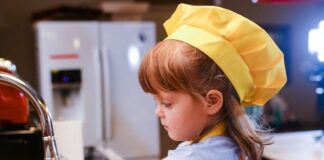 Una niña con delantal amarillo delante de un fregadero, lista parece para ponerse a cocinar
