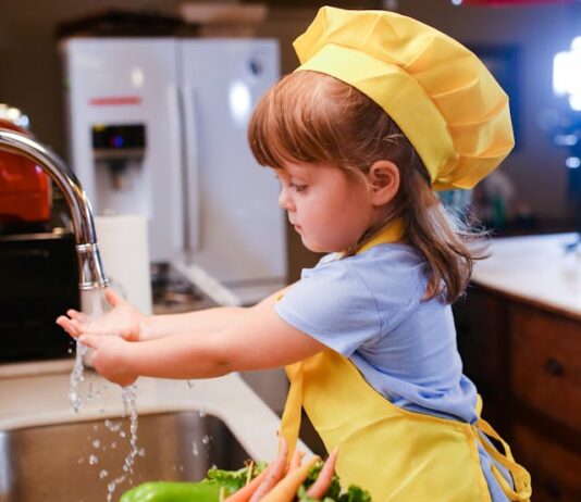 Una niña con delantal amarillo delante de un fregadero, lista parece para ponerse a cocinar
