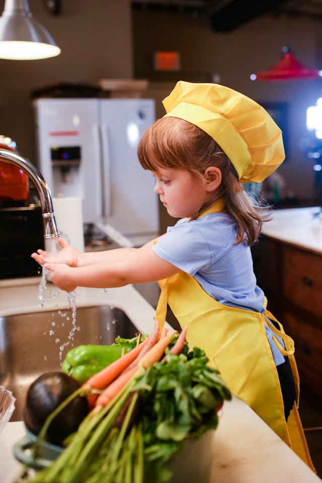 Una niña con delantal amarillo delante de un fregadero, lista parece para ponerse a cocinar