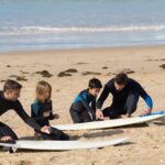 Niños con instructor en la arena, preparándose para hacer surf