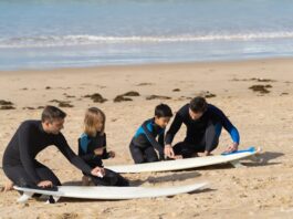 Niños con instructor en la arena, preparándose para hacer surf