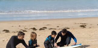 Niños con instructor en la arena, preparándose para hacer surf