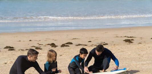 Niños con instructor en la arena, preparándose para hacer surf