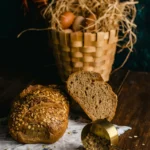 Espelta, trigo integral y avena: ¿qué cereal impacta menos en la glucemia? Panes rústicos de avena e integral sobre una mesa de madera con una cesta de huevos