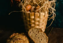 Espelta, trigo integral y avena: ¿qué cereal impacta menos en la glucemia? Panes rústicos de avena e integral sobre una mesa de madera con una cesta de huevos