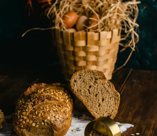 Espelta, trigo integral y avena: ¿qué cereal impacta menos en la glucemia? Panes rústicos de avena e integral sobre una mesa de madera con una cesta de huevos