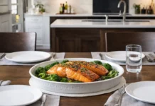 Mesa elegante servida para dos en una cocina luminosa, con platos vacíos y una fuente central con salmón al horno recién preparado listo para compartir.