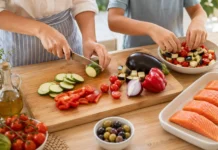 Salmón al horno con verduras mediterráneas y aceitunas salteadas Manos de una cocinera y un niño preparando salmón al horno con calabacín, berenjena, pimiento rojo, cebolla y tomates cherry.