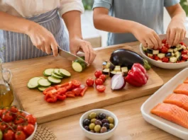 Salmón al horno con verduras mediterráneas y aceitunas salteadas Manos de una cocinera y un niño preparando salmón al horno con calabacín, berenjena, pimiento rojo, cebolla y tomates cherry.