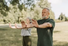 Dos personas adultas practican Tai Chi al aire libre en un parque, una actividad suave y de bajo impacto adecuada para mejorar equilibrio y movilidad.
